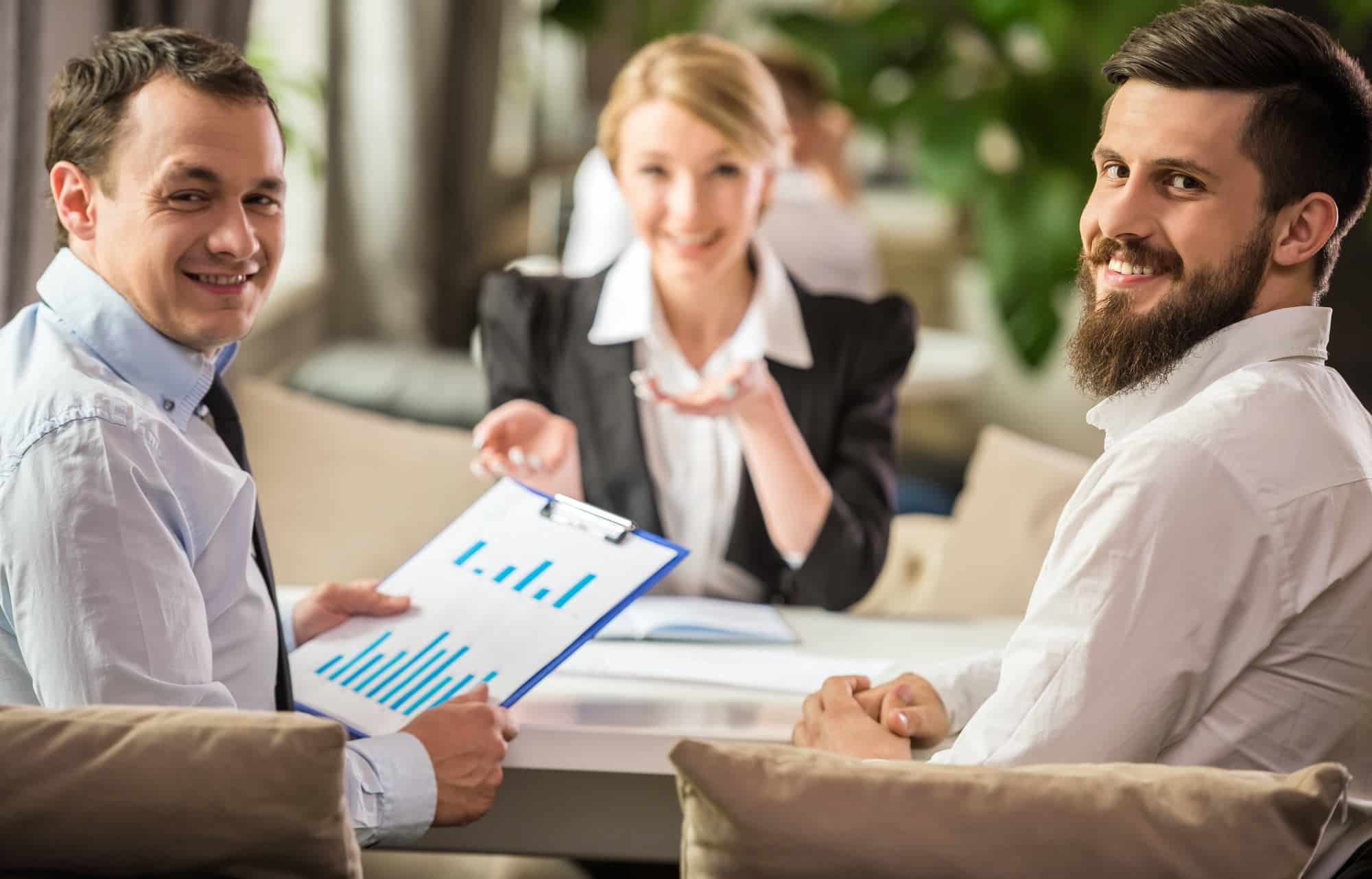 Trois personnes discutent autour d'une table, examinant les détails d'un contrat d'assurance pour établir un devis personnalisé pour un client.